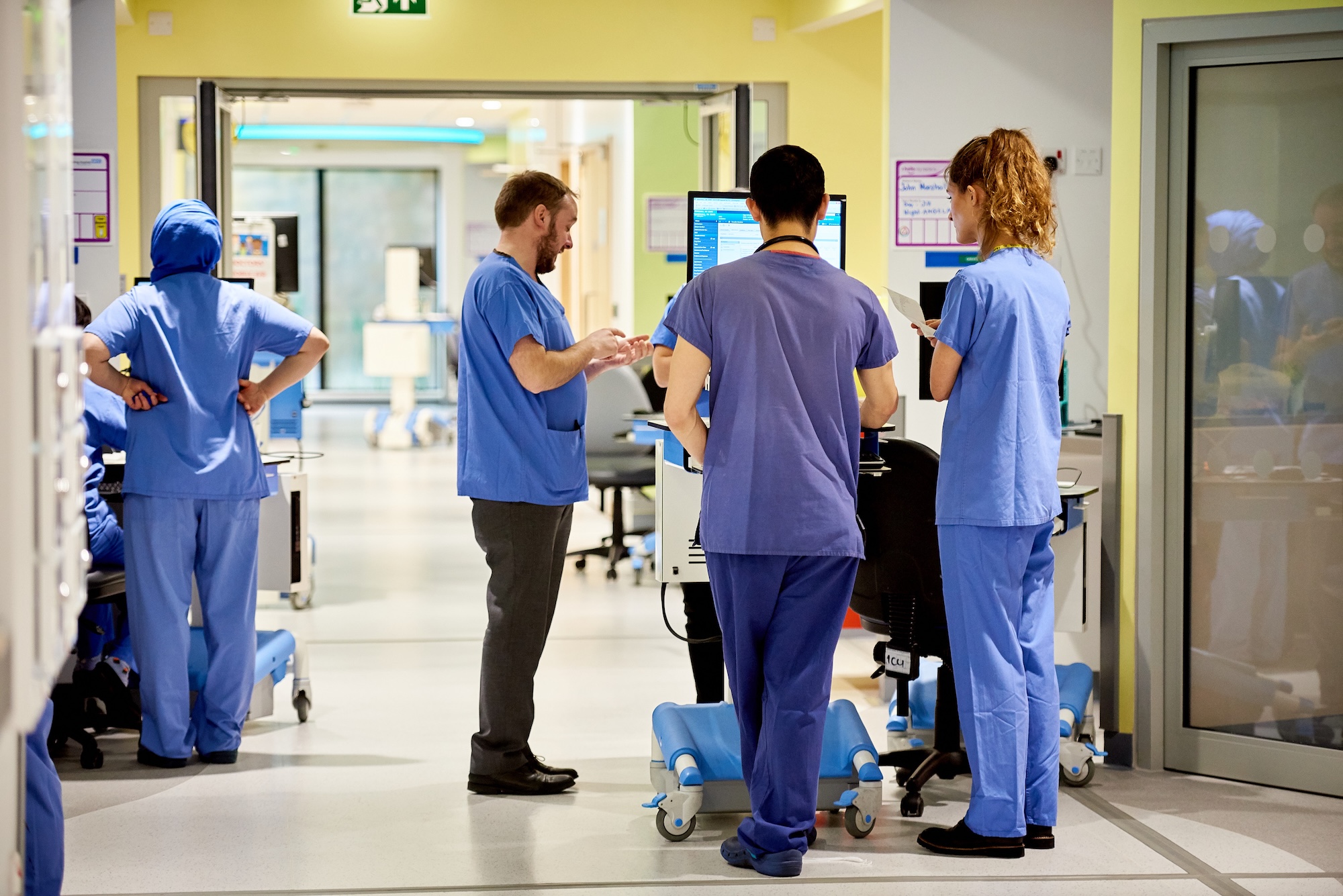 A hospital corridor with medical professionals working there wearing blue scrubs
